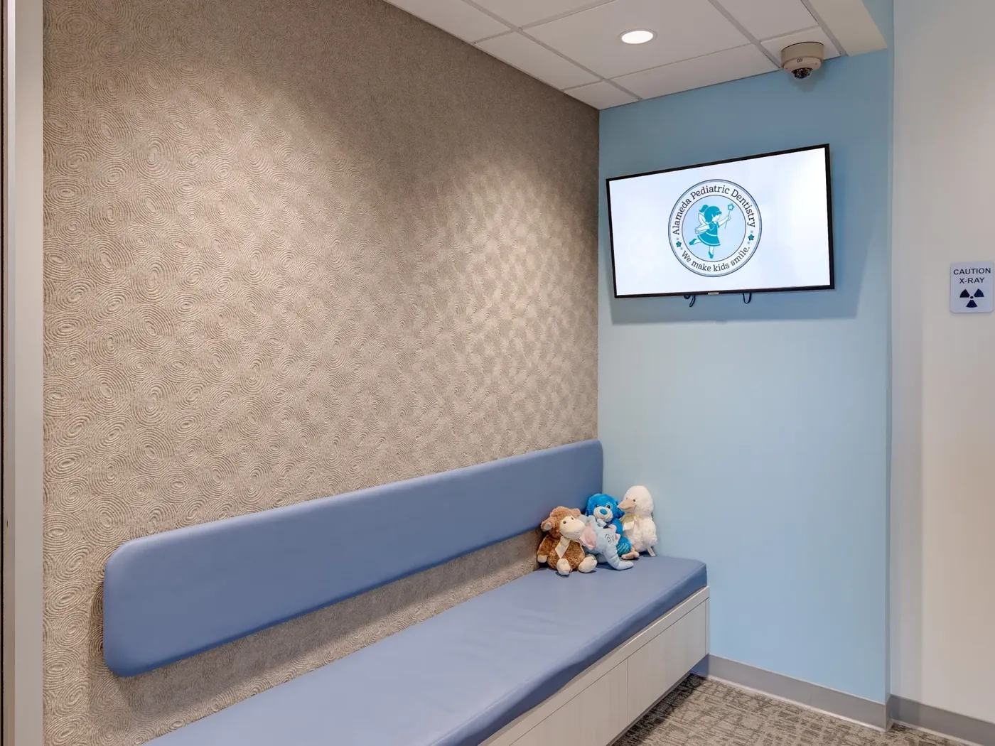 A waiting area bench with a wall-mounted screen showing the practice logo