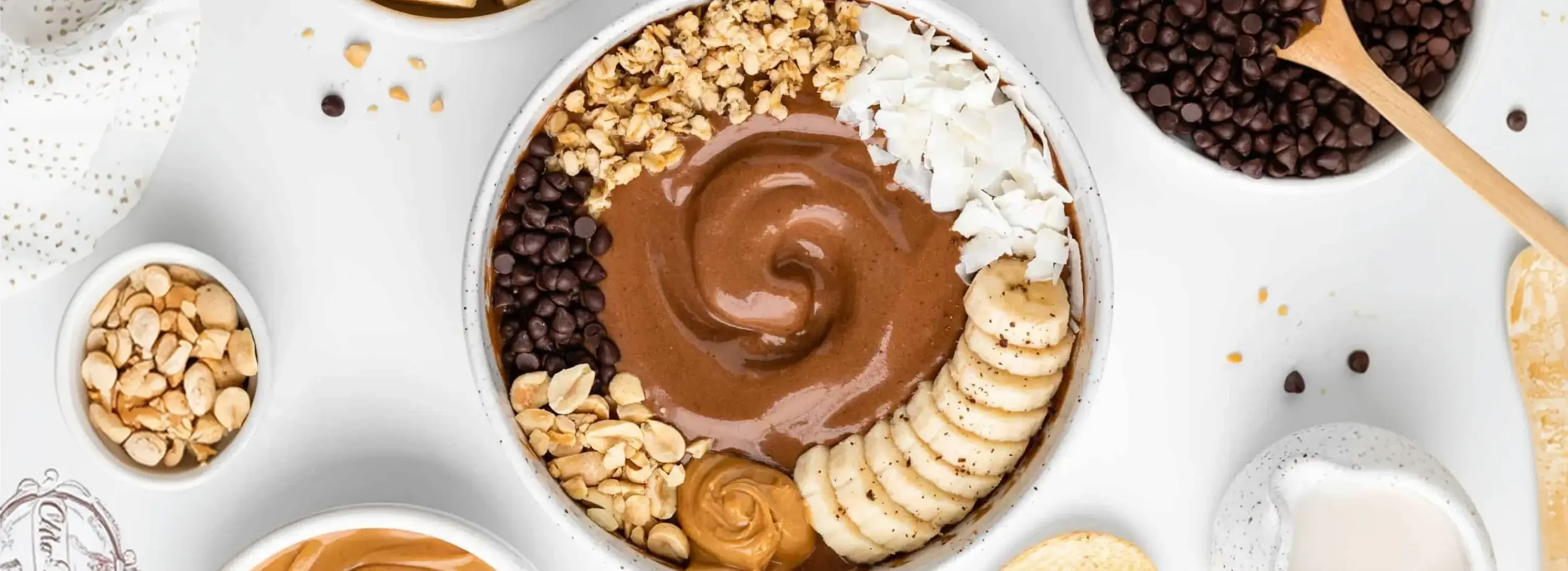 A chocolate peanut butter smoothie bowl topped with banana slices, granola, coconut, and chocolate chips