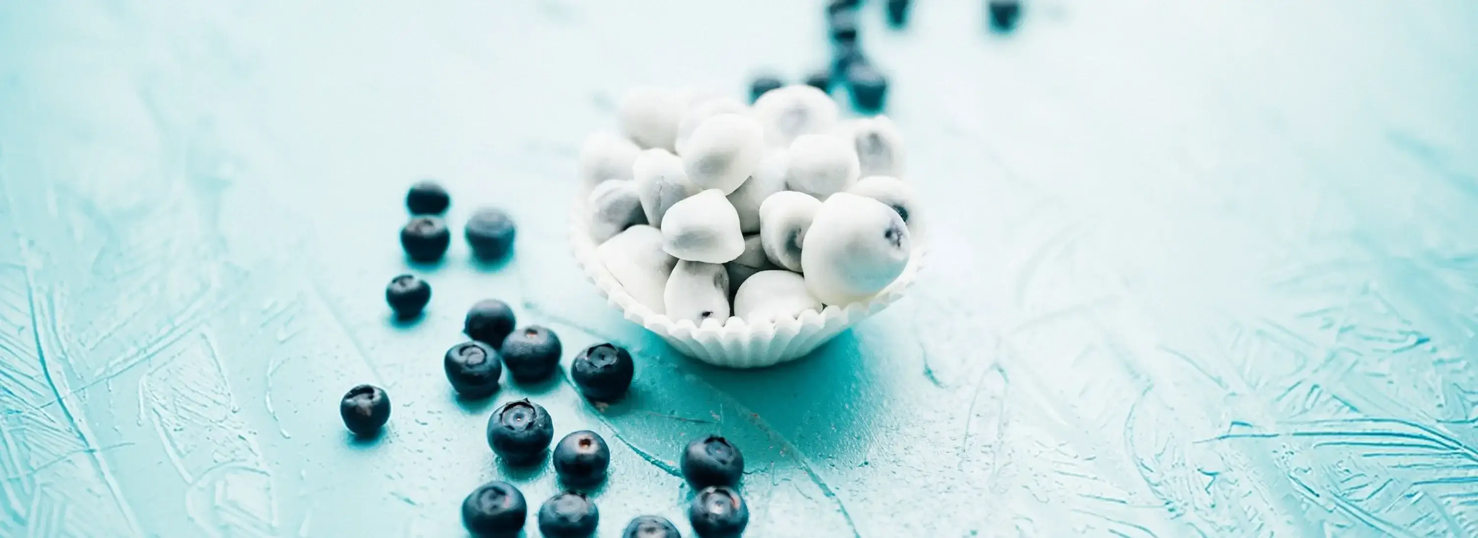 A bowl of yogurt-covered frozen blueberries surrounded by fresh blueberries