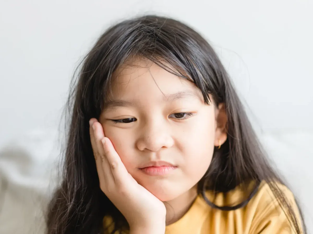 A young girl holding her cheek in discomfort from tooth pain